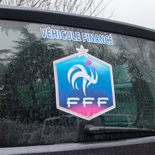 Sticker du logo FFF collé sur la vitre arrière d’un véhicule, avec la mention « Véhicule financé ».