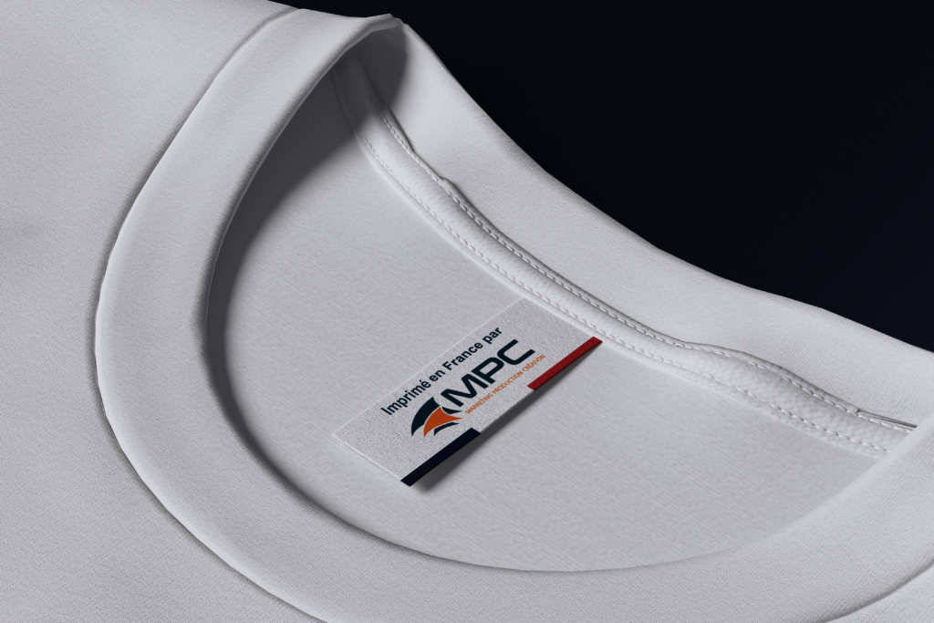 Étiquette tissée cousue à l'intérieur du col d'un t-shirt blanc, portant le logo MPC et la mention "Fabriqué en France par MPC – Marketing Production Création", avec un drapeau français.