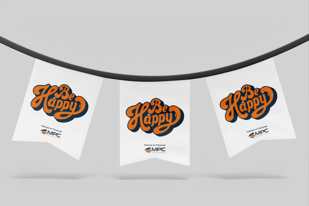 Guirlande de trois fanions blancs suspendus à un fil noir, imprimés du message "Be Happy" en typographie rétro orange et bleu marine, avec la mention "Fabriqué en France par MPC" en bas de chaque fanion.