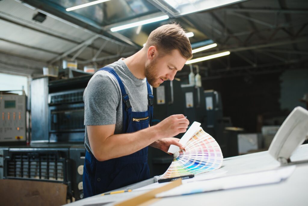 Opérateur vérifiant les couleurs d’une impression à l’aide d’un nuancier dans un atelier d’impression.